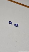 Pair of pear-shaped purple blue tanzanite gemstones on a neutral background. Good focus on colour and cut showing clarity and shape.