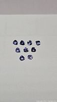 Photo showing nine loose blue-purple tanzanite gemstones arranged on a white surface under light showing their color and clarity.