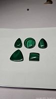 Five polished Malachite stones of various shapes arranged on a white background, clearly showing their patterns and shine.