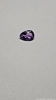 Close-up photo of single pear cut Bolivian amethyst gemstone on a neutral background, showcasing its color, cut, and clarity.