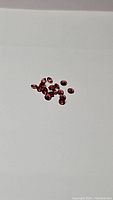 Multiple small calibrated red-orange garnet gemstones scattered on a white background, showing faceted oval shapes and deep red-orange color.