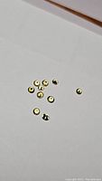 Photo showing a group of 10 small round yellow sapphires with diamond cut facets on a white surface.
