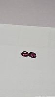 Two oval cut electric purple to hot pink untreated tourmaline gemstones shown from a distance on white background.