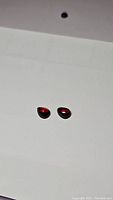 Two pear-shaped deep cherry red garnet cabochon gemstones placed side by side on a white background, showing their smooth polished surfaces and rich color.