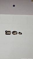 Three loose smokey quartz gemstones arranged side by side on a white background showing emerald, oval, and round cuts in light brown color.