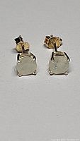 Close-up image of both silver post earrings with square rainbow moonstone gemstones in four-prong settings, lying on a flat surface, showing earring backs.