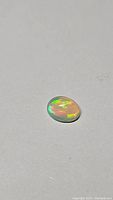 Oval cabochon cut Ethiopian opal gemstone with vivid flashes of green and yellow color.