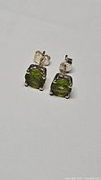 Close-up view of the pair of square shaped apple green peridot earrings mounted in 925 sterling silver, showing metal and stone details.