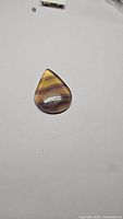 Single teardrop-shaped polished purple fluorite cabochon with banded colors, shown on white background.