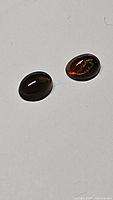 Close up photo of two oval-shaped untreated black opals on a plain light background showing vivid flashes of color
