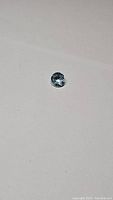 Top view photo of a single natural round cut sky blue topaz gemstone on a plain background.