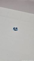 Close-up photo showing oval cut natural Swiss blue topaz gemstone on white background with visible internal transparency and blue hue.