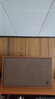 Front view of a vintage Noresco floor speaker showing wooden frame and woven fabric grille with Noresco logo badge.