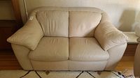 Front view of beige Italian leather loveseat sofa with two cushions and padded armrests, slightly worn and marked.