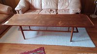 Full front view of long rectangular teak coffee table on light rug with sofa background