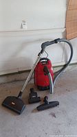Full lot showing red canister vacuum, hose, wand and three attachments.