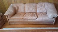 Full front view of the tan leather sofa showing three cushions and wooden floor.