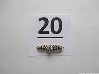 Full view of the gold brooch pinned to a white tag labelled 20, showing overall size and design.