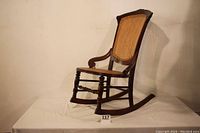 Side view of antique Victorian armless rocking chair showing wood frame, curved rockers, and cane seat and back.