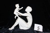 Side profile showing mother sitting with baby held up in front reaching forward.