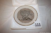 Full view of the ceramic plate stored in foam packaging showing the plate with lion, menorah and Star of David design on white background.