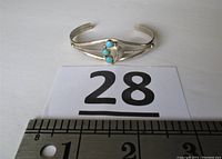 Front view of silver-tone cuff bracelet with three turquoise stones placed on ruler showing measurement