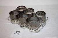 Top and angled front view of six iridescent green and clear highball glasses arranged in a stainless steel carrying rack.