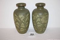 Front view of both matching olive green vases showing detailed raised floral vine pattern with gilded edges