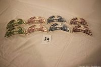 Six bone dishes in three colors arranged in two rows. Each color has two crescent-shaped dishes patterned with transfer print designs.