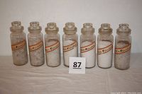 Seven vintage glass apothecary bottles labeled 'Natr. Chloratum' arranged in a row containing different sizes of salt crystals.