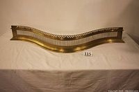 Full view of the solid brass fireplace fender on a cloth surface showing wave design and decorative pierced top border