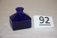 Front and top view photo of the cobalt blue glass ink bottle shaped like a schoolhouse with embossed window and roof details.