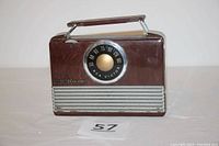 Front view of the brown RCA Victor portable radio with metal handle, tuning dial, and speaker grill.
