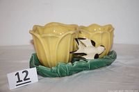 Front angled view of the double yellow tulip planter on green leaf base showing the attached swallow figure.