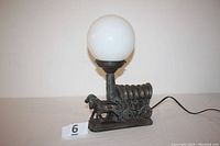 Front view of the vintage lamp showing horses and covered wagon base with globe on top.