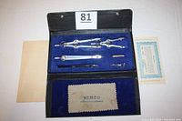 Open black case with blue velvet interior displaying five metal drafting tools, a parts list, and a cloth with Vemco branding.