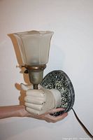 View of wall lamp showing white hand holding frosted glass shade and speckled circular base.