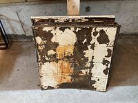 Stack of tin ceiling tiles showing peeling paint, rust, and wear.