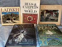 Photo showing five large coffee table books about Eastern regions: Ladakh, Rugs & Carpets of the World, Kashmir, Iran, and Persia by Roloff Beny.