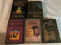 Five hardcover books by Elizabeth Peters arranged in two rows on a fabric surface, showing front dust jacket covers.