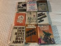 Nine Isaac Asimov hardcover books arranged in three rows showing fronts with dust jackets. Condition and titles visible.