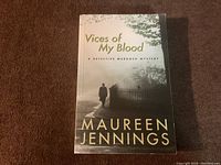 Front cover of 'Vices of My Blood' showing title, author's name, and cover art with a person walking by a fence in a foggy outdoor setting.