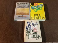 Three books by Paul Theroux laid out on fabric surface showing covers: Sunrise with Seamonsters, The Mosquito Coast, World's End and Other Stories.