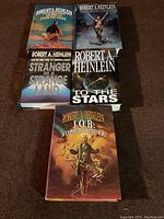 Five hardcover books by Robert A. Heinlein with dust jackets laid out on floor.