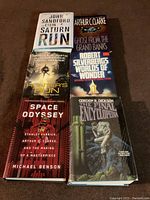Six hardcover science fiction books laid out on floor: 'Saturn Run,' 'Ghost from the Grand Banks,' 'Hunter's Run,' 'Worlds of Wonder,' 'Space Odyssey,' and 'The Final Encyclopedia.' Shows condition and dust jackets.