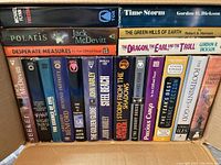 Photo showing an assortment of science fiction books standing upright in a box, featuring titles and author names on colorful spines.