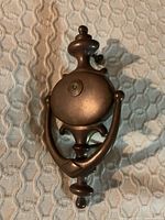 Full view of the solid brass antique door knocker showing the knocker handle and top finial with a circular peep hole on the oval base plate.