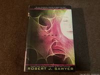 Front cover of the first edition hardcover book 'Wake' by Robert J. Sawyer. Abstract colored smoke design with a pale face partially visible.