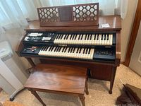 Front view of the Baldwin electronic organ with bench visible underneath, showing dual keyboards and control panel.
