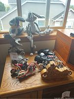 Wide view showing Bugs Bunny plush, multiple Bugs Bunny figurines, metal motorcycle replicas, wooden motorcycle puzzle, and eagle figurine on wooden surface by window